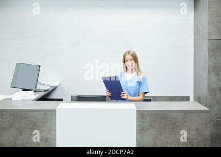 Glückliche junge hübsche Assistentin oder Rezeptionistin in blauer Uniform stehend Nach Zähler Stockfoto