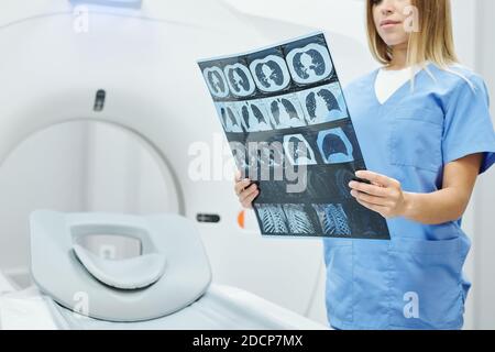 Junge Radiologin in blauer Uniform hält Röntgenbild von Kopf des Patienten Stockfoto