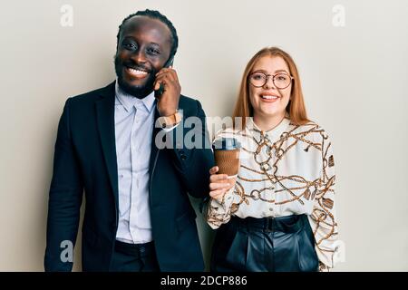Junge interracial paar mit Smartphone und trinken eine Tasse Kaffee sieht positiv aus und glücklich stehen und lächeln mit einem Selbstbewusstes Lächeln Stockfoto