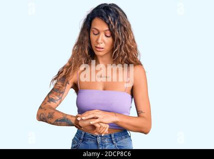 Junge hispanische Frau mit Tattoo tragen lässige Kleidung Überprüfung der Zeit auf Armbanduhr, entspannt und zuversichtlich Stockfoto