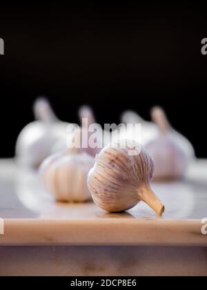 Knoblauchzwiebeln auf einer Marmorplatte mit Betonung auf der vorderen Glühbirne geschossen. Stockfoto