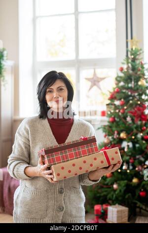 Glücklich reif Brünette Frau in Casualwear halten geschenkboxen mit Geschenken Stockfoto