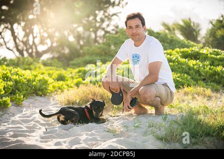 Junge fit männlichen Kniebeugen am Strand mit seinem kleinen Schwarzer Hund auf Hawaii Stockfoto