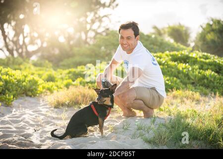 Junge fit männlichen Kniebeugen am Strand mit seinem kleinen Schwarzer Hund auf Hawaii Stockfoto