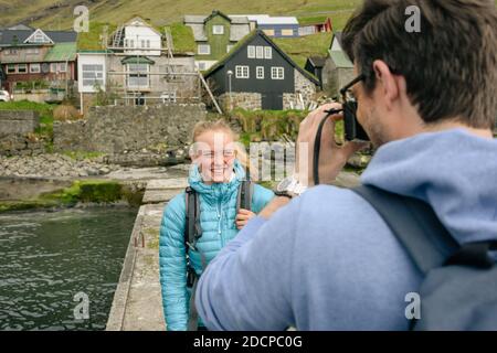 Männlicher Fotograf, der glückliche weibliche Touristen auf Pier in der Nähe der Küste schießt Abrechnung Stockfoto