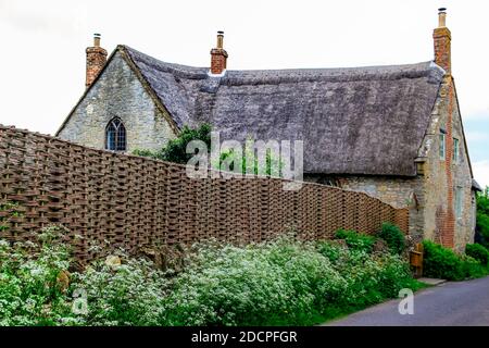 Ein meisterhaft gewebter Wasserzaun umgibt den Garten eines historisch bedeutsamen und schönen Reetdachhauses in East Coker, Somerset, England Stockfoto