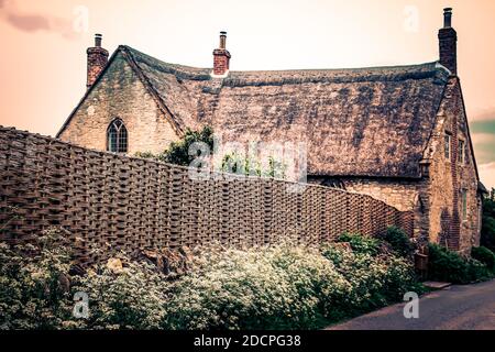 Ein meisterhaft gewebter Wasserzaun umgibt den Garten eines historisch bedeutsamen und schönen Reetdachhauses in East Coker, Somerset, England Stockfoto