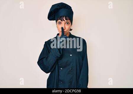 Schöne brunettte Frau trägt professionelle Koch Uniform fragen, ruhig mit Finger auf den Lippen zu sein. Stille und geheime Konzept. Stockfoto