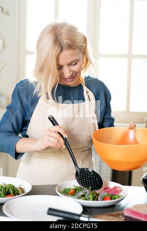 Blonde reife weibliche Putting gedämpfte grüne Bohnen auf Teller mit Fleisch und Salat Stockfoto