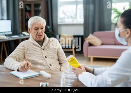 Senior Mann in Casualwear Blick auf Flasche Pillen in Hände des jungen Arztes Stockfoto