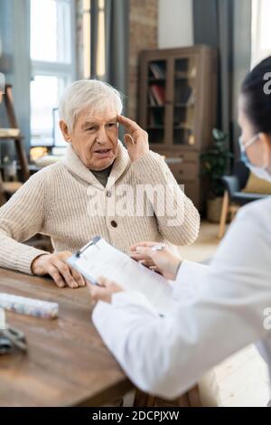 Kranke ältere Mann in Casualwear Blick auf junge Ärztin In Whitecoat Stockfoto