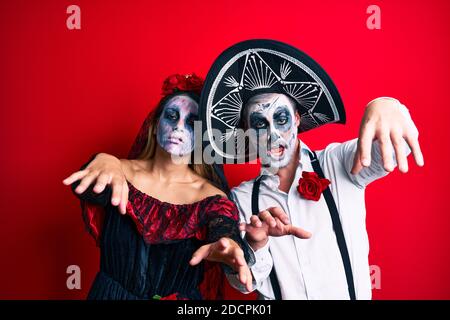 Schönes Paar trägt Tag der Toten Kostüm gestikuliert als Zombie über isolierten roten Hintergrund. Stockfoto