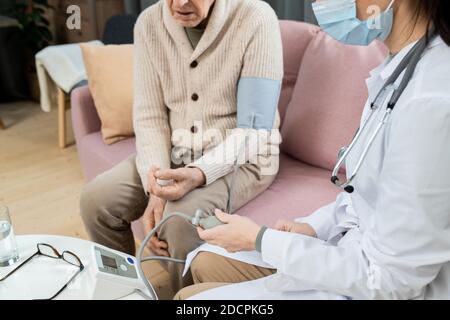 Junge Ärztin in Whitecoat Messung des Blutdrucks von Kranken Älterer Herr Stockfoto