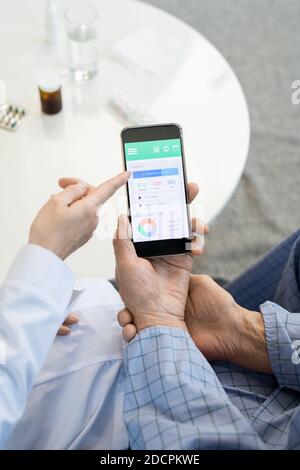 Die Hände der jungen Ärztin im Weißkochspalt zeigen auf das Display Des Smartphones Stockfoto