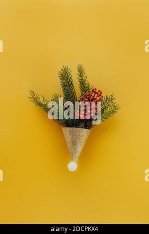 Festliche Weihnachtskomposition in dekorativer glänzender goldener Mütze mit Fichte Zweige und trockene Beeren und Kegel auf trendigen leuchtend goldenen Gelber Hintergrund Stockfoto