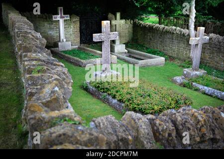 Gut gepflegter alter versunkener Friedhof mit steinernen Kreuzen, die mit Mauern umgeben sind Trockener Stein und scharfe Kapselsteine im historischen Stil in St. Michael & All Angels Kirche in Stockfoto