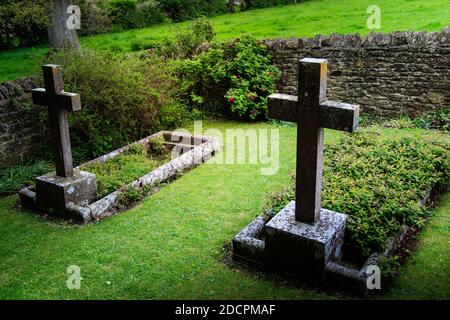 Gut gepflegter alter versunkener Friedhof mit steinernen Kreuzen, die mit Mauern umgeben sind Trockener Stein und scharfe Kapselsteine im historischen Stil in St. Michael & All Angels Kirche in Stockfoto