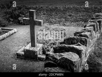 Gut gepflegter alter versunkener Friedhof mit Steinkreuzen, die mit trockenem Stein und scharfen Kapselsteinen in der St. Michael & All Angels Church in East Coker, England, gemauert sind Stockfoto