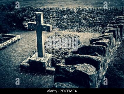 Gut gepflegter alter versunkener Friedhof mit Steinkreuzen, die mit trockenem Stein und scharfen Kapselsteinen in der St. Michael & All Angels Church in East Coker, England, gemauert sind Stockfoto