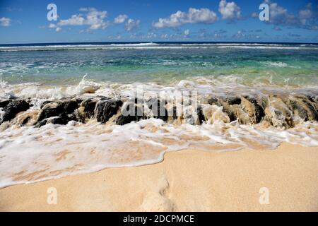 Ozeanwellen, die über Lava-Rifffelsen, Sandstrand, blaues Meer, Himmel und Wolken in Guam, Mikronesien verschüttet werden Stockfoto
