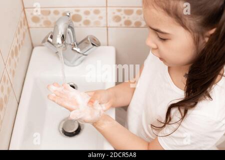 Ein kleines Brünette Mädchen wäscht ihre Handflächen über dem Waschbecken im Badezimmer mit einer Flut von Wasser. Stockfoto