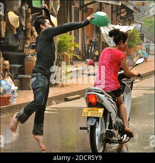 Junger Mann wirft Wasser über einen vorbeifahrenden Motorradfahrer während Songkran Wasserwerfen Festival. Stockfoto