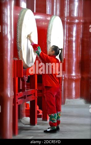 Seitenansicht eines chinesischen Mädchens, das eine riesige traditionelle Trommel spielt. Stockfoto