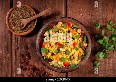 Couscous, ein flaches Lay Shot in einem Tagine mit Zutaten, auf einem dunklen Holzhintergrund Stockfoto