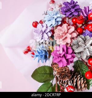 Weihnachtliche Dekoration, Bouquet aus Tannenzapfen und roten Beeren. Rosa Hintergrund, Draufsicht, Nahaufnahme. Zapfen in verschiedenen Farben lackiert. Stockfoto