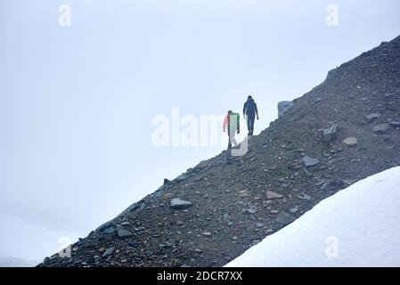 Rückansicht von männlichen Reisenden mit Rucksäcken, die in Bergen unter hellblauem Himmel wandern. Tapfere Freunde Bergsteiger zu Fuß auf felsigen Hügel. Konzept von Reisen, Wandern und aktiver Freizeit. Stockfoto