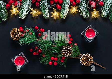 Weihnachtlicher Hintergrund mit grünen Fichtenzweigen, Tannenzapfen und Stechbeeren auf schwarzem Hintergrund. Festliche Vorlage, Postkarte mit Tannenzweigen und de Stockfoto