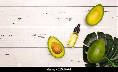 Avocado-Öl in einer Glasflasche mit einer Pipette, Avocado geschnitten. Kosmetik für Körper-, Gesichts-, Haut- und Haarpflege. Spa-Anlage. Blick von oben, heller Holzhintergrund Stockfoto