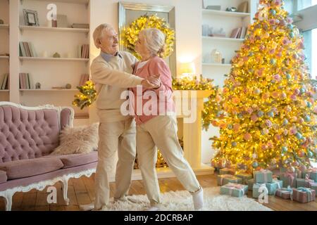 Seniorenpaar tanzt in der Nähe von Neujahr Baum und sieht glücklich aus Stockfoto