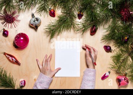Weibliche Hände Schreiben Brief an den Weihnachtsmann und alte Vintage Weihnachtsbaum Ornamente und Kiefernäste auf hellem Holzhintergrund. Stockfoto