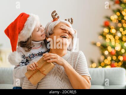 Frohe Weihnachten und schöne Feiertage! Fröhliche Oma und ihre niedliche Enkelin Mädchen tauschen Geschenke. Oma und kleines Kind Spaß in der Nähe von Baum ich Stockfoto