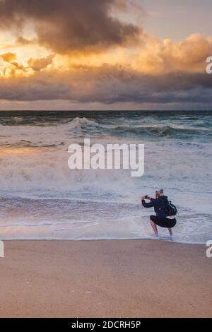 Ein Urlauber, der mit seinem Handy einen spektakulären Sonnenuntergang über Fistral Beach in Newquay in Cornwall fotografiert. Stockfoto