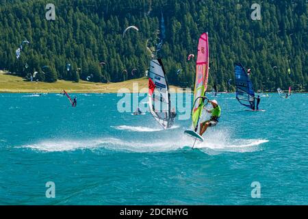 Windsurfer mit bunten Segeln segeln auf dem Silvaplana See. Stockfoto