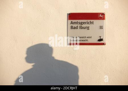 23. November 2020, Niedersachsen, Bad Iburg: Ein Justizbeamter wirft einen Schatten auf eine Mauer am Landgericht. An der Wand hängt ein Schild mit der Aufschrift 'Amtsgericht Bad Iburg - dieser Bereich steht unter Videoüberwachung'. Ein Beklagter hat sich für einen Verstoß gegen das Tierschutzgesetz zu verantworten. Insgesamt sollen drei beschuldigte Fahrer (unabhängig voneinander) Tiere in das Schlachthaus in Bad Iburg transportiert haben, obwohl sie aufgrund von Verletzungen und/oder Krankheit nicht mehr transportiert werden konnten. Die Verletzungen waren den Fahrern bekannt (siehe dpa 'Versuche zur Tierquälerei im Schlachthof Stockfoto