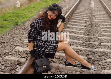 Frau in schwarzem Kleid, Hut und Handschuhe sitzen auf Bahngleise Stockfoto