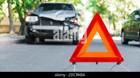 Rotes Not-aus-Dreieck-Schild auf der Straße bei einem Autounfall. Gebrochenes graues Auto während des Verkehrsunfalls. Autounfall Verkehrsunfall auf der Stadtstraße Stockfoto