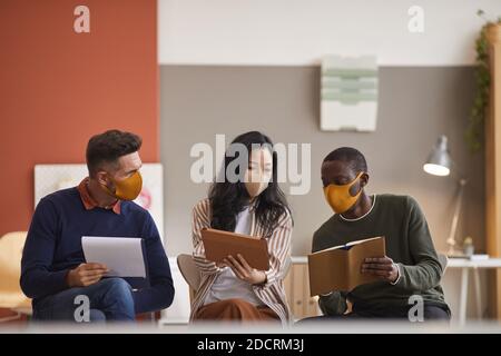 Multi-ethnische Gruppe von drei Geschäftsleuten tragen Gesichtsmasken während Besprechung des Projekts im Büro Stockfoto