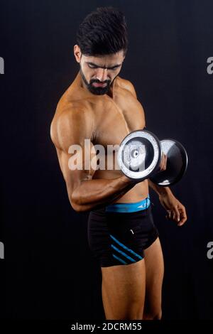 Muskulösen Bodybuilder männlich in der Turnhalle. Schwarzer Hintergrund. Vorderprofil. Blick nach unten. Zeigt Brust- und Armmuskulatur. Tragegewichte Stockfoto