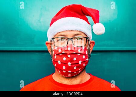 Portrait von erwachsenen kaukasischen Mann trägt rote Schutzmaske für Coronavirus vocid-19 und santa claus chrismtas Hut - Konzept der Menschen allein während ho Stockfoto