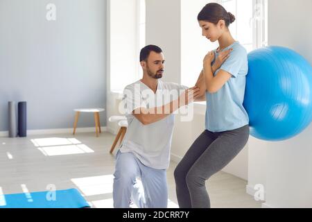 Männliche Physiotherapeutin hilft weiblichen Patienten, Übungen mit Fitness-Ball in Physiotherapie-Raum zu tun. Stockfoto