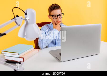 Home Schulbildung und Fernunterricht für Kinder. Nachdenkliche intelligente Schüler am Tisch sitzen, Lernen durch Video-Link mit dem Lehrer, auf einem Yello Stockfoto