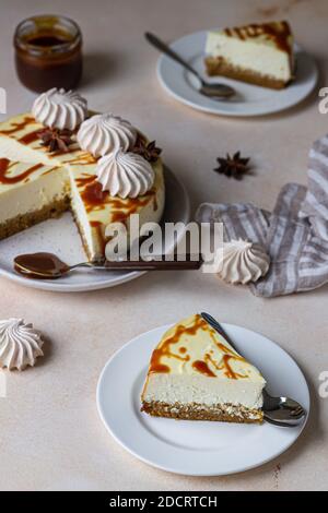 Stück Karotten-Vanille-Käsekuchen mit gesalzenem Karamell-Belag und Baiser auf einer weißen Keramikplatte, heller Betonhintergrund. Selektiver Fokus. Stockfoto