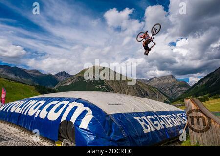 Ein Downhill-Radfahrer übt einen schwierigen Sprung mit der Sicherheit der Landung auf einem großen Airbag im Mottolino Bike Park, die Berge von Livi umgeben Stockfoto