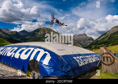 Ein Downhill-Radfahrer übt einen schwierigen Sprung mit der Sicherheit der Landung auf einem großen Airbag im Mottolino Bike Park, die Berge von Livi umgeben Stockfoto