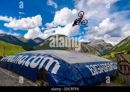 Ein Downhill-Radfahrer übt einen schwierigen Sprung mit der Sicherheit der Landung auf einem großen Airbag im Mottolino Bike Park, die Berge von Livi umgeben Stockfoto