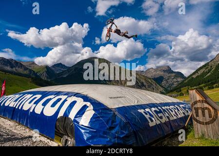 Ein Downhill-Radfahrer übt einen schwierigen Sprung mit der Sicherheit der Landung auf einem großen Airbag im Mottolino Bike Park, die Berge von Livi umgeben Stockfoto